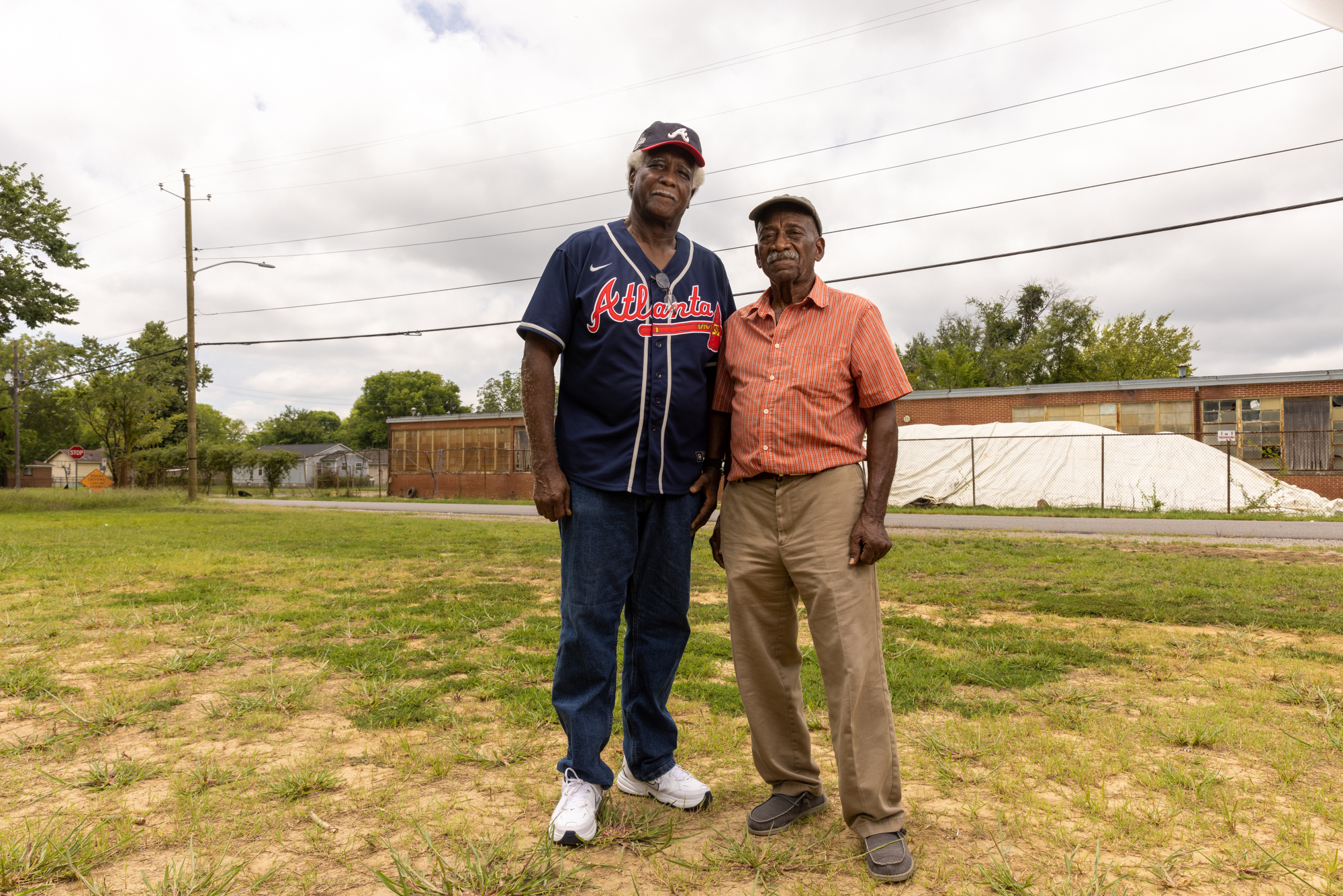 Longtime Collegeville residents Chester Wallace (left) and Jimmy Smith (right) stand in front of the former Carver High School. After the EPA excavates contaminated soil from properties in the Superfund site, the agency stores it under a white tarp until it can be hauled away to a disposal site. Credit: Lynsey Weatherspoon for ProPublica